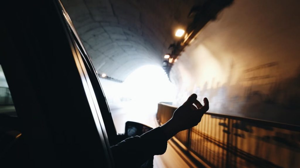 A hand extends out of a car window while driving through a brightly lit tunnel.