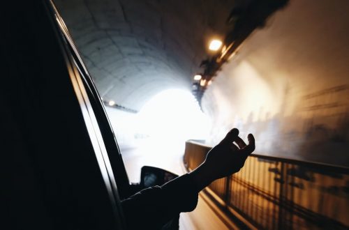 A hand extends out of a car window while driving through a brightly lit tunnel.